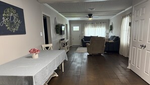 Ein geräumiges Wohnzimmer mit Essbereich, Holzboden und Deckenventilator.