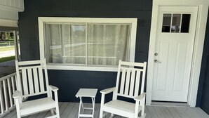Eine Veranda mit zwei weißen Schaukelstühlen und einem kleinen Tisch, ein Fenster mit weißem Rahmen und eine weiße Tür.