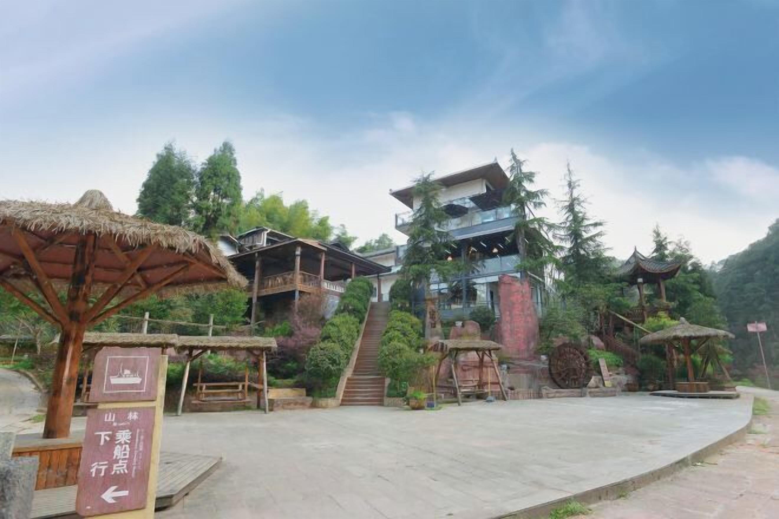 Ein traditionelles Gebäude mit einer Treppe, die zu einer höheren Ebene führt, umgeben von Grünflächen und einem Gebäude mit Strohdach.