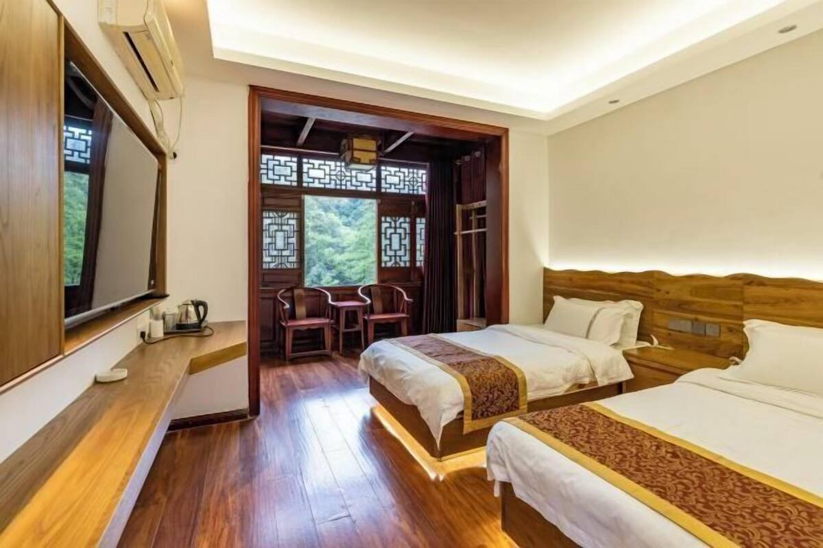 A bedroom with a wooden headboard, a bed with white bedding, a bedside table with a kettle, and a view through a window with a decorative screen.