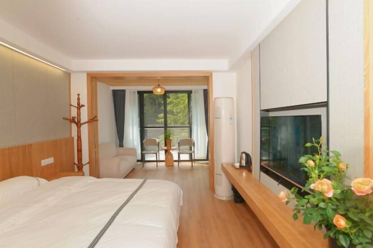 A modern hotel room with a bed, a TV, a desk, and a view of the outdoors.