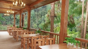 A wooden deck with tables and chairs, surrounded by dense forest. - Shanlin Holiday Hotel (Chongqing)