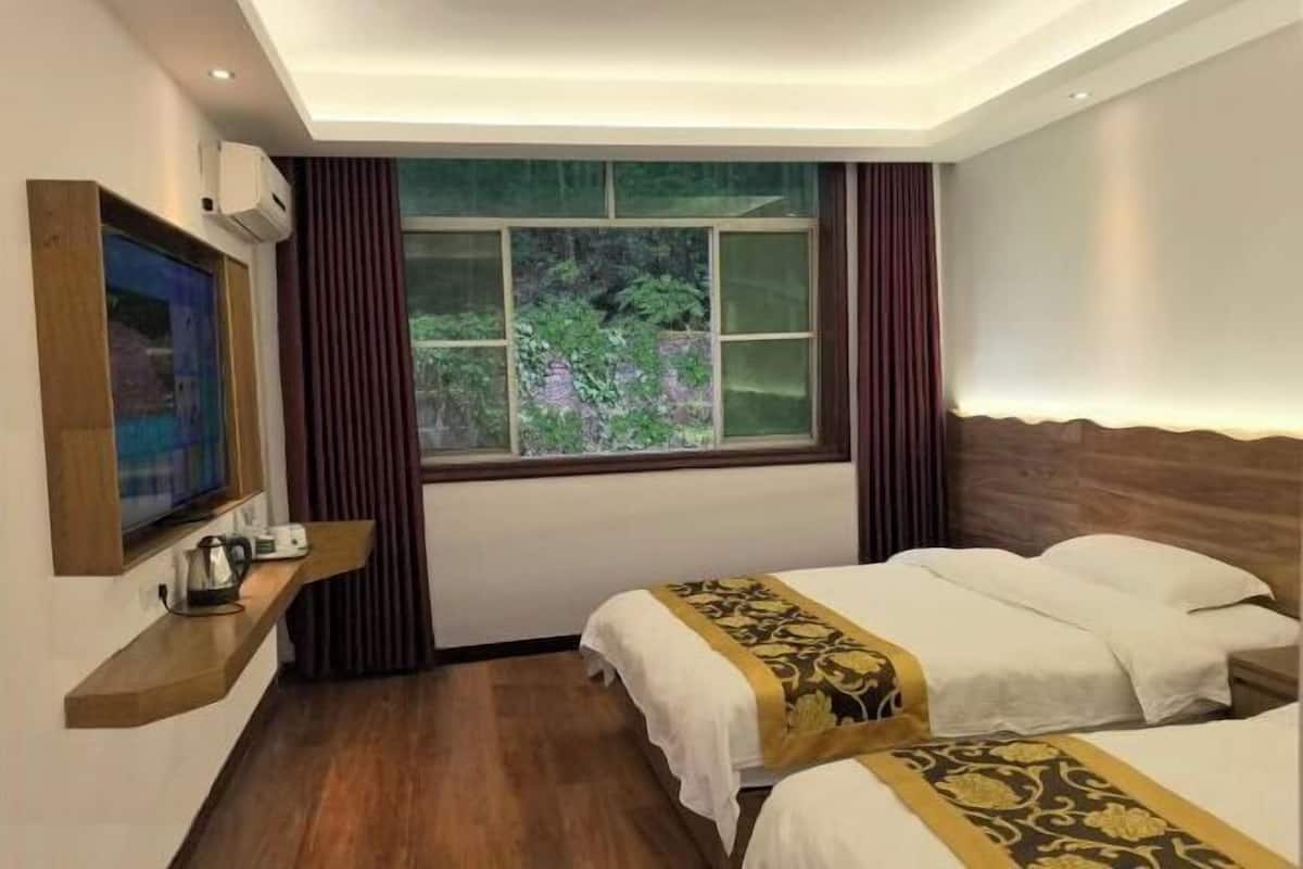 A hotel room with two beds, a TV, a window with curtains, and a wooden shelf with a kettle.