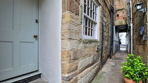 A narrow alleyway with a stone building, a white door, and a potted plant. - The Gull's Nest (Whitby)