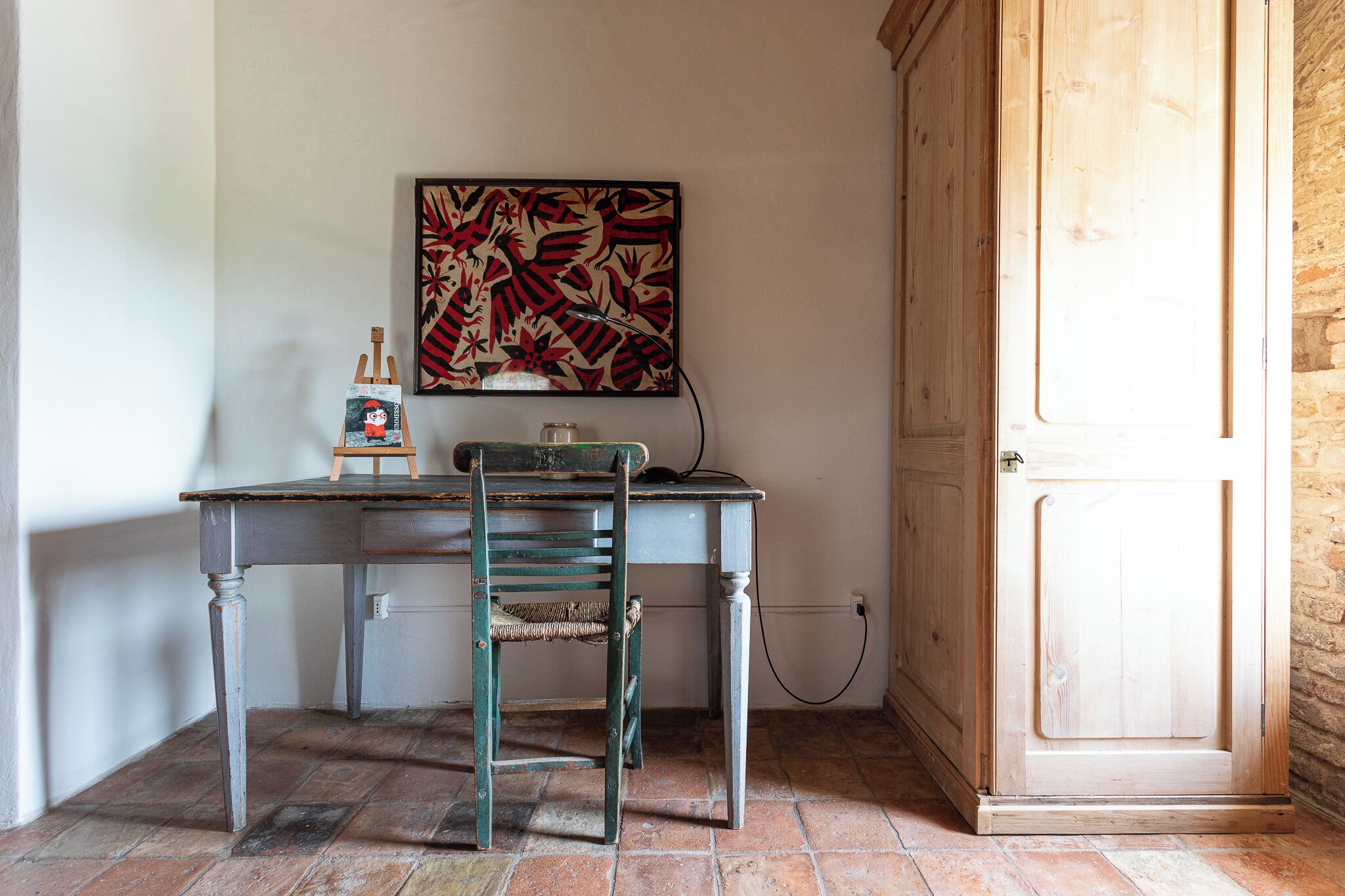 Ein Zimmer mit einem Holztisch, einem Stuhl und einem großen, abstrakten Gemälde an der Wand.