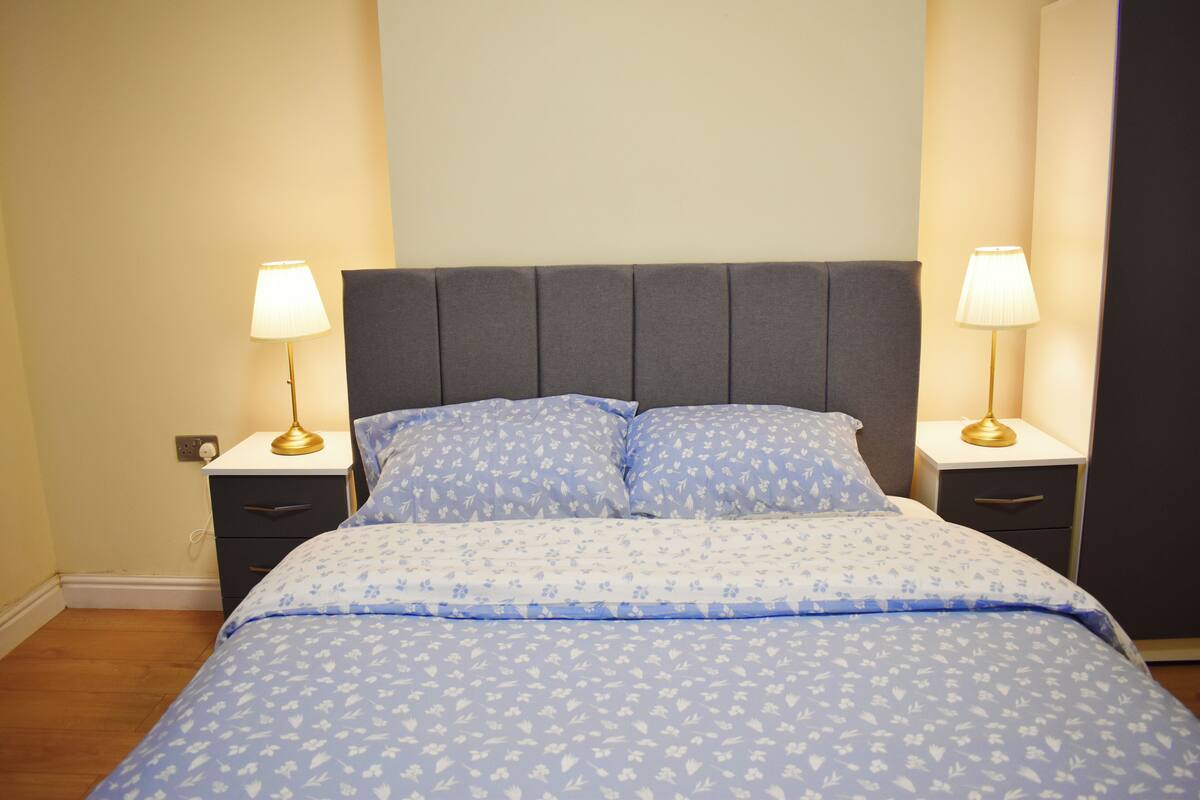 Um quarto com uma cama, duas mesas de cabeceira e duas luminárias.