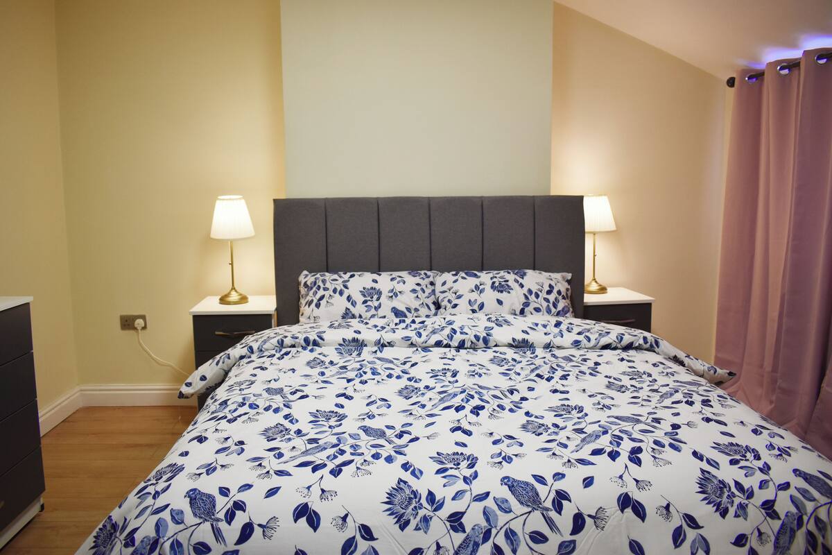 Um quarto com uma cama, duas mesas de cabeceira e um criado-mudo.