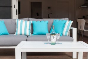 A living room with a grey sofa adorned with blue and white striped pillows, a white coffee table in front, and a bottle of wine with two glasses on it.