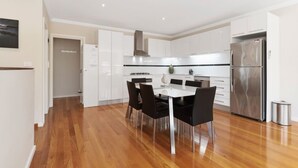 A modern kitchen with white cabinets, a stainless steel refrigerator, and a dining table with chairs. - Beach Walk Apartment (Safety Beach)