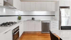 A modern kitchen with white cabinetry, a gas stove, a dishwasher, and a refrigerator. - Beach Walk Apartment (Safety Beach)
