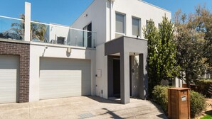 A modern two-story house with a garage, a balcony, and a small garden area. - Beach Walk Apartment (Safety Beach)