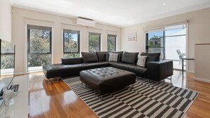 A modern living room with a sectional sofa, a glass coffee table, and a striped rug. - Beach Walk Apartment (Safety Beach)
