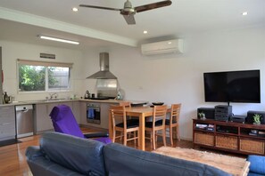 A modern kitchen with a dining area, a large flat-screen TV, and a ceiling fan. - Rustic Rye Beach House (Rye)