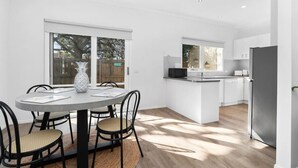 Una cocina moderna con armarios blancos, un refrigerador de acero inoxidable y una zona de comedor con una mesa redonda y sillas.