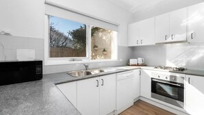 Una cocina moderna con armarios blancos, microondas integrado, fregadero, estufa y ventana con vistas a árboles.