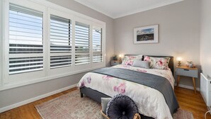Un dormitorio con una cama grande, una mesita de noche, un cuadro en la pared y una ventana con persianas.