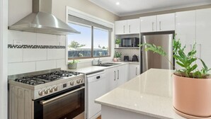 Una cocina moderna con armarios blancos, electrodomésticos de acero inoxidable y un amplio ventanal que proporciona luz natural.