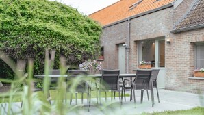 A patio with a table and chairs, a brick building, and a large bush.