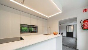 A modern kitchen with a white countertop, stainless steel appliances, and a window with a view of greenery.