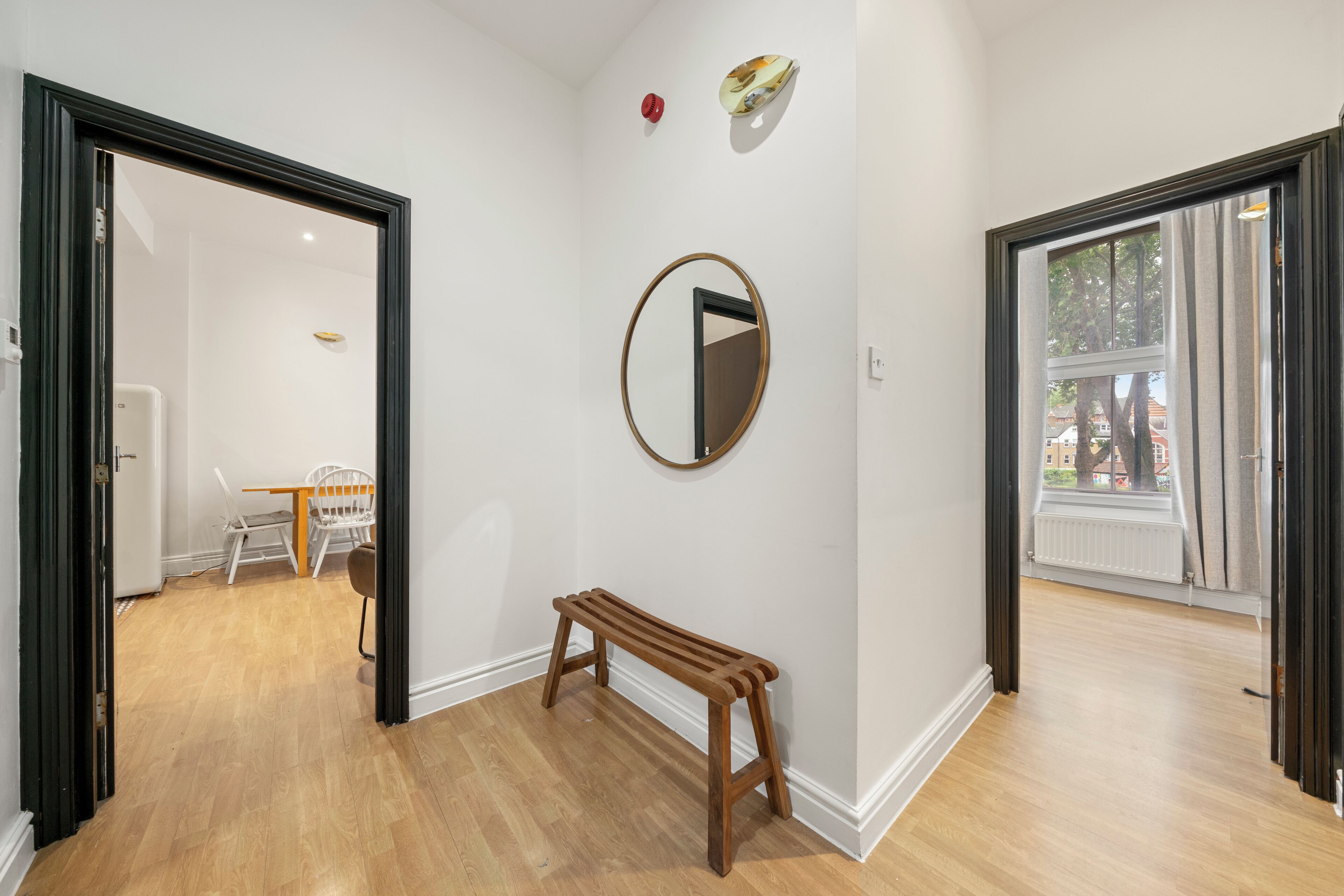 Un couloir avec un banc en bois, un miroir rond accroché au mur et un coin repas comprenant une table et des chaises.