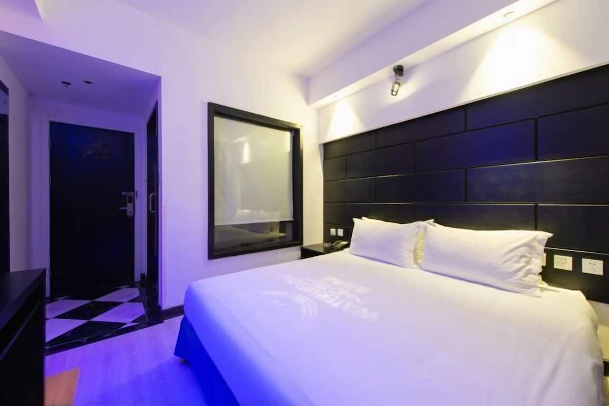 A hotel room with a large bed, a desk, a chair, a wardrobe, and a door.