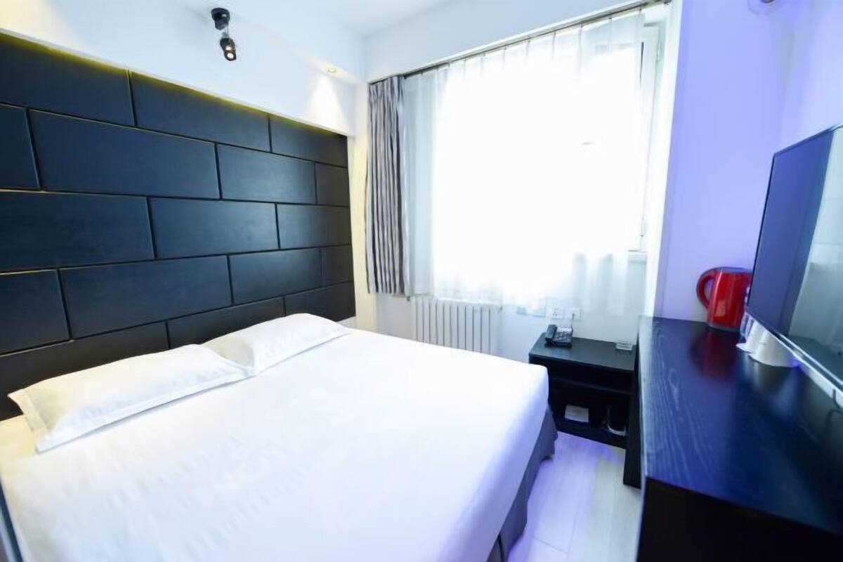 A hotel room with a bed, a TV, a desk, and a window with curtains.