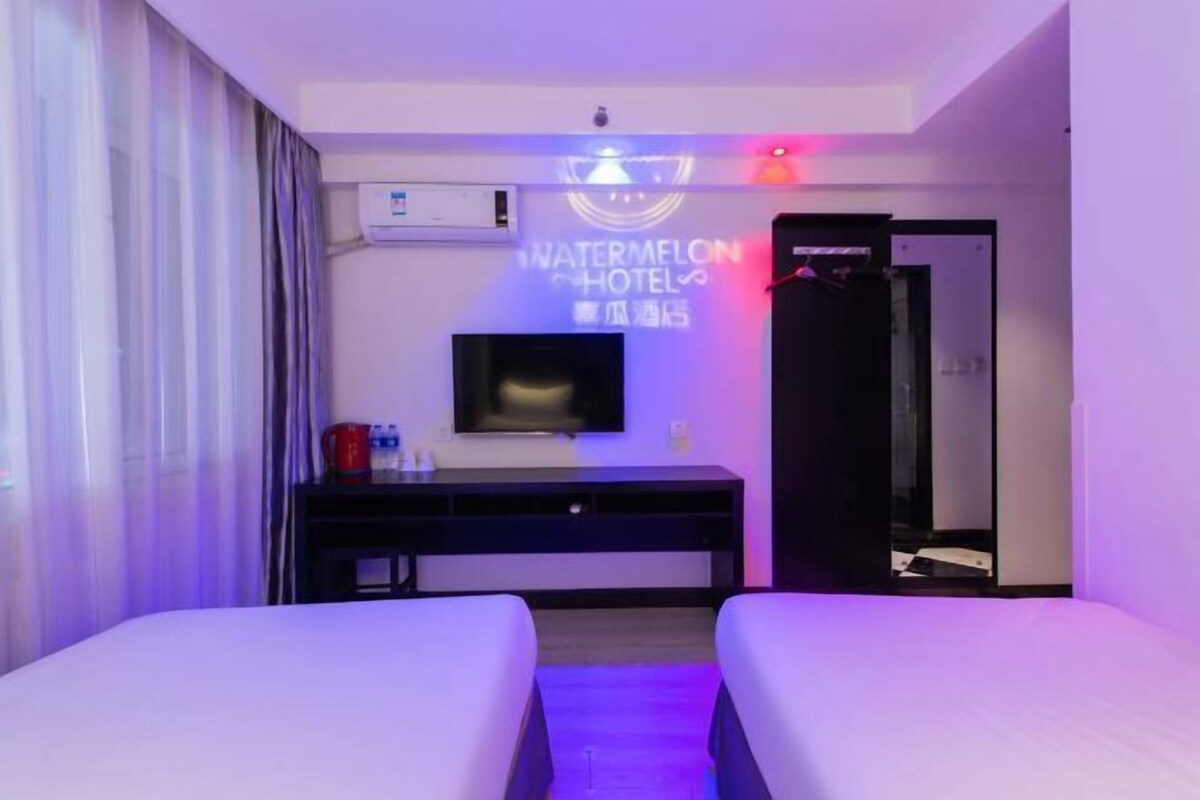 A hotel room with a bed, a desk, a TV, and a neon sign.