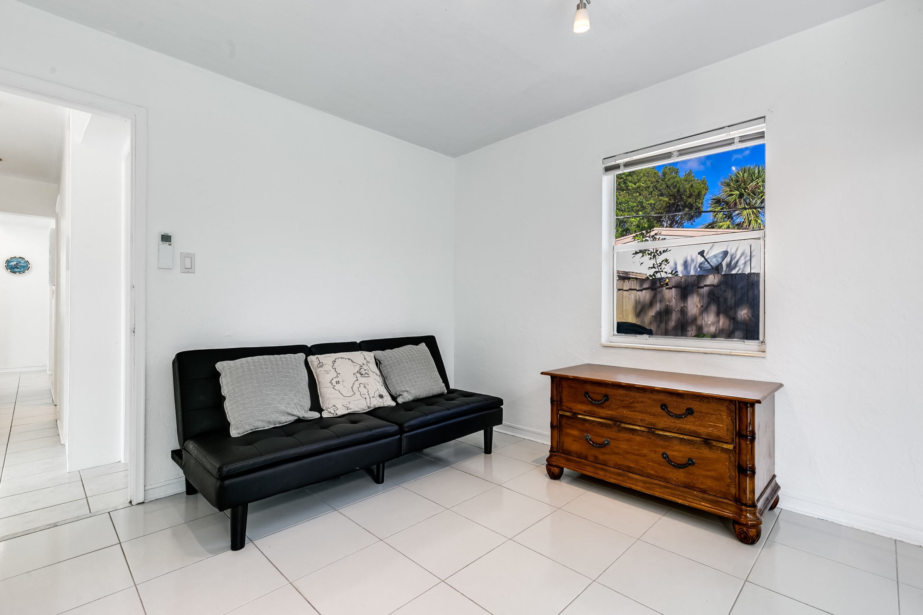 Ein Zimmer mit einer schwarzen Couch, einem Holzkasten und einem Fenster mit Blick auf Bäume und einer Satellitenschüssel.