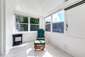 A room with a single green polka dot chair, a small table, and large windows with a view of greenery and a building. - Bungalow with large backyard, 5 min from beach (Pompano Beach)