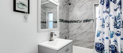 Un baño con lavamanos blanco, espejo, ducha e inodoro.