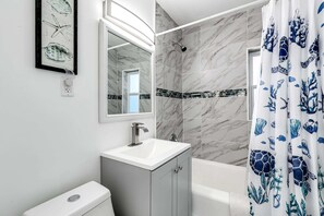 Une salle de bain avec un lavabo blanc, un miroir, une douche et des toilettes.