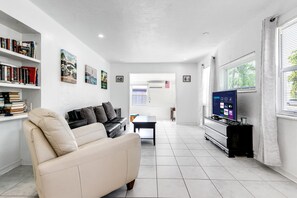 A modern living room with a beige sofa, a TV on a stand, and bookshelves filled with books.
