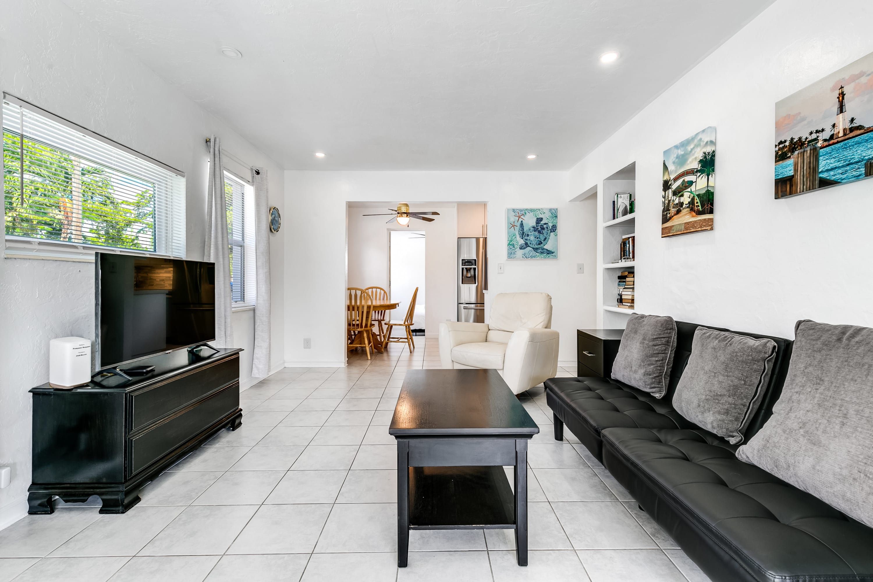 Un salon moderne avec un téléviseur à écran plat, un canapé foncé, une table basse et un coin repas à l’arrière-plan.