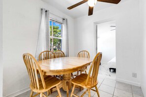 Un coin repas avec une table et des chaises en bois, un ventilateur de plafond et une fenêtre avec des rideaux.