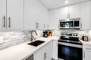 A modern kitchen with white cabinets, a stainless steel microwave, a stove, and a sink.