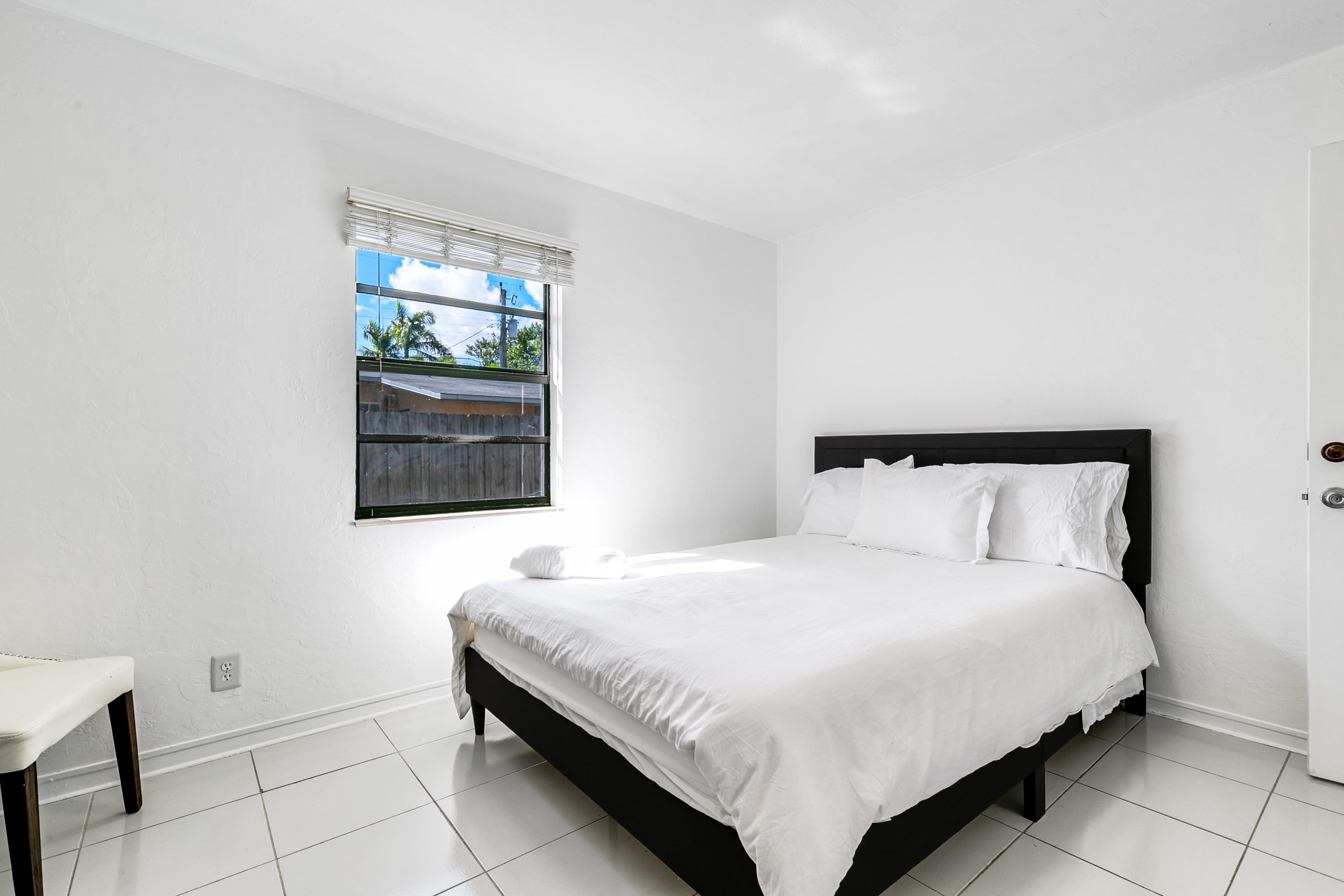 A bedroom with a bed, a window with blinds, and a white wall.