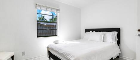 A bedroom with a bed, a window with blinds, and a white wall.