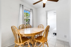 A dining area with a wooden table and chairs, a window with curtains, and a ceiling fan. - Bungalow with large backyard, 5 min from beach (Pompano Beach)