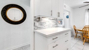 Une cuisine moderne avec des armoires blanches, un plan de travail blanc et un pare-feu en carreaux. On y trouve une table à manger avec des chaises et un miroir accroché au mur.
