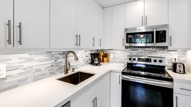 Une cuisine moderne avec des meubles blancs, un four à micro-ondes en acier inoxydable, une cuisinière et un évier.