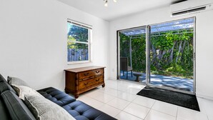 Un salon moderne avec un canapé, un meuble en bois et une grande porte-fenêtre coulissante donnant sur un jardin.