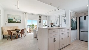 Eine moderne Küche mit einer zentralen Kochinsel, einem Essbereich mit einer Couch und Sesseln, sowie Kunstwerken an den Wänden.