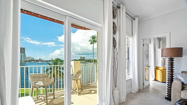 Ein Balkon mit Blick auf das Meer und die Stadt, ein Korbstuhl, eine Couch und eine Lampe.