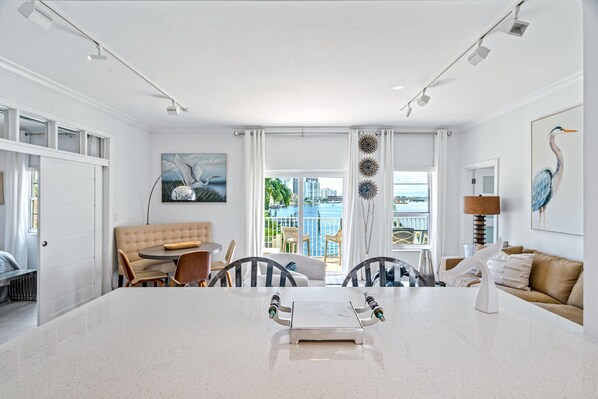 A modern hotel room with a large white marble table, a beige sofa, and a balcony with a view of the city and water. - Walk to Ft Lauderdale beach - Water Views & Pool (Fort Lauderdale)