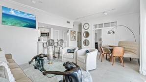 Ein modernes Wohnzimmer mit einem Glastisch, einem beigen Sofa und einem Essbereich mit rundem Tisch und Stühlen.