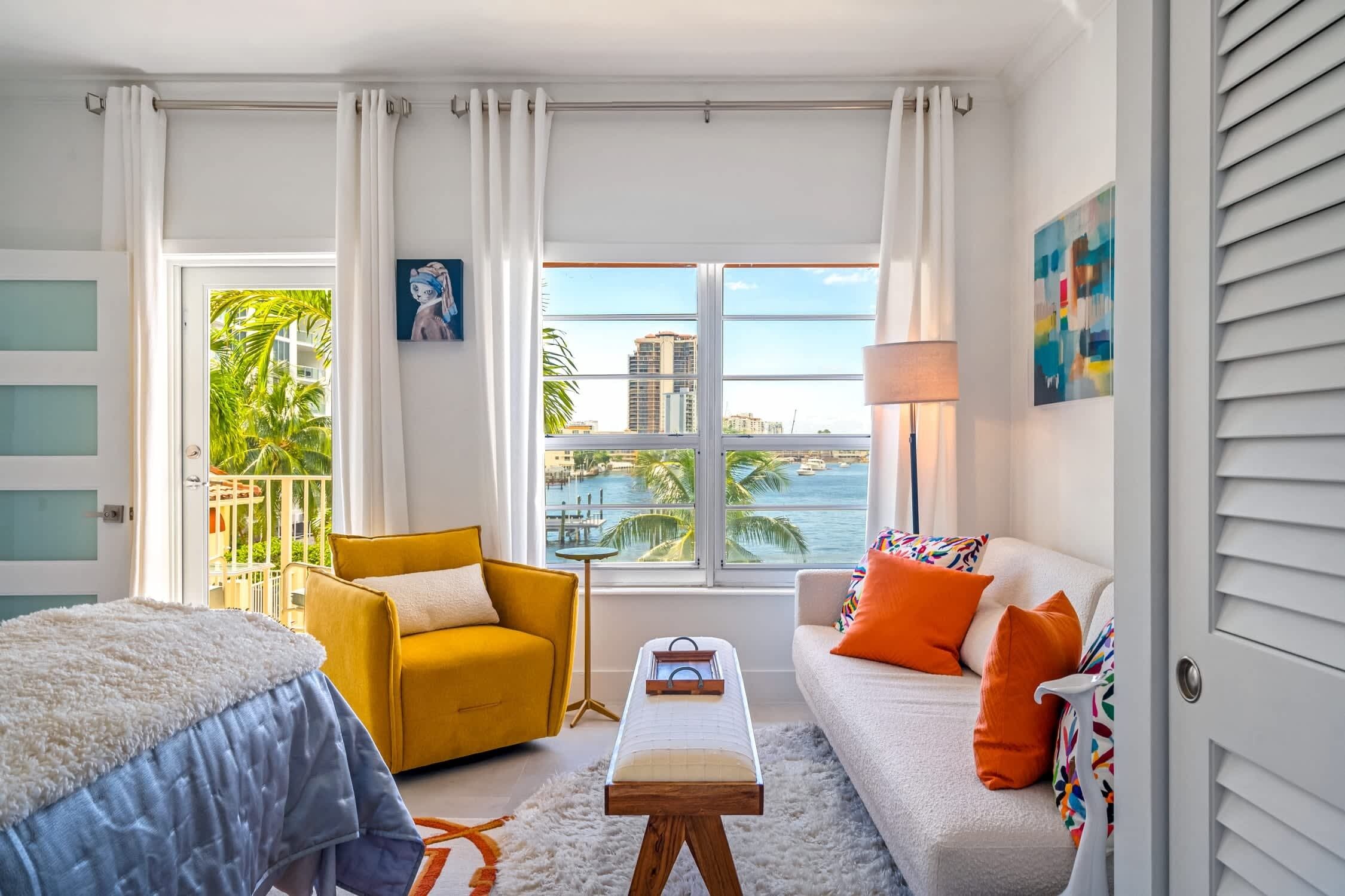 Una sala de estar moderna con un sofá, un sillón amarillo y vistas al océano a través de amplios ventanales.