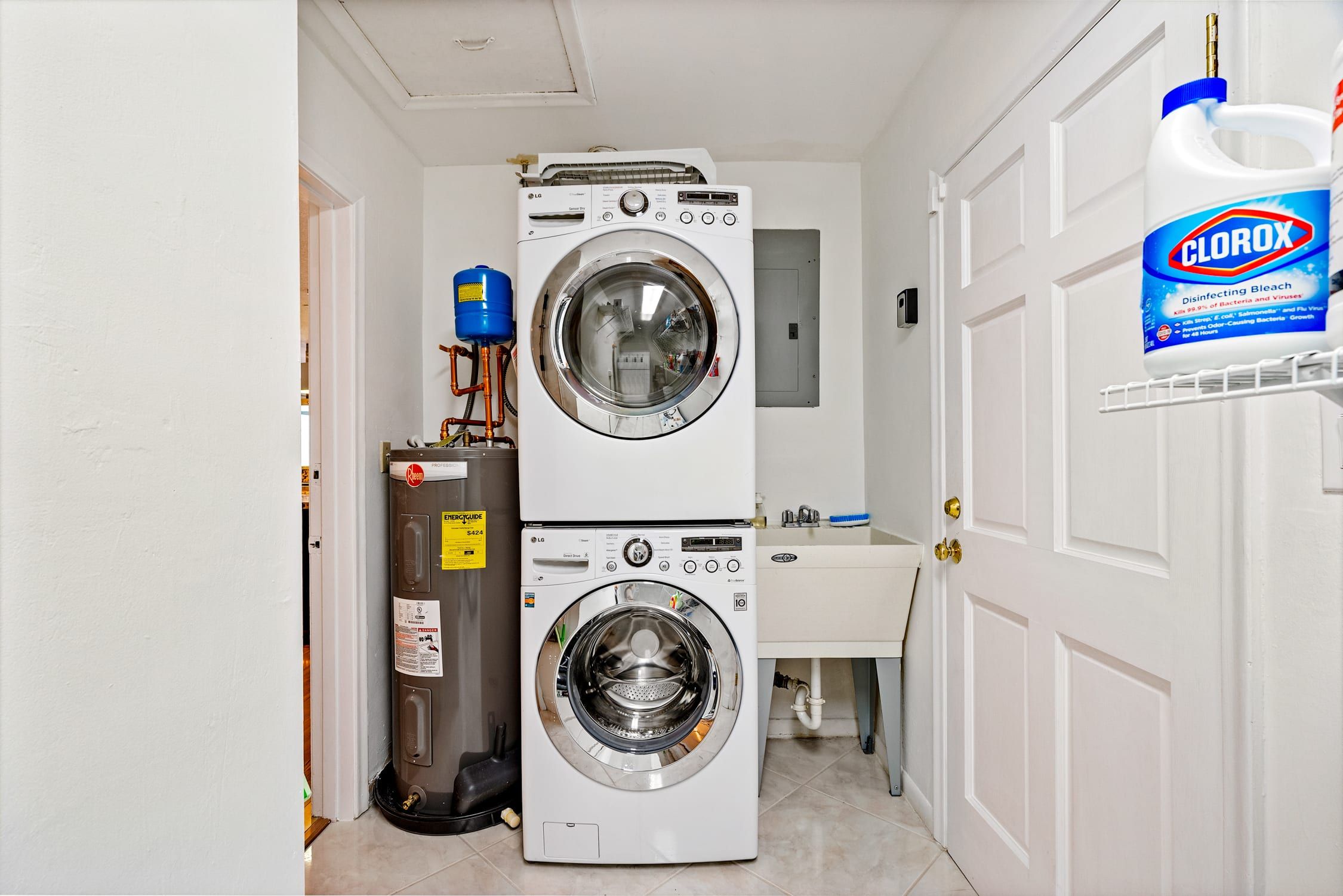 A laundry room with two stacked washing machines, a water heater, and a Clorox disinfecting bleach bottle.