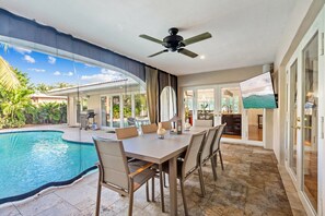 A poolside dining area with a table and chairs, a ceiling fan, and a view of the pool and outdoor space.