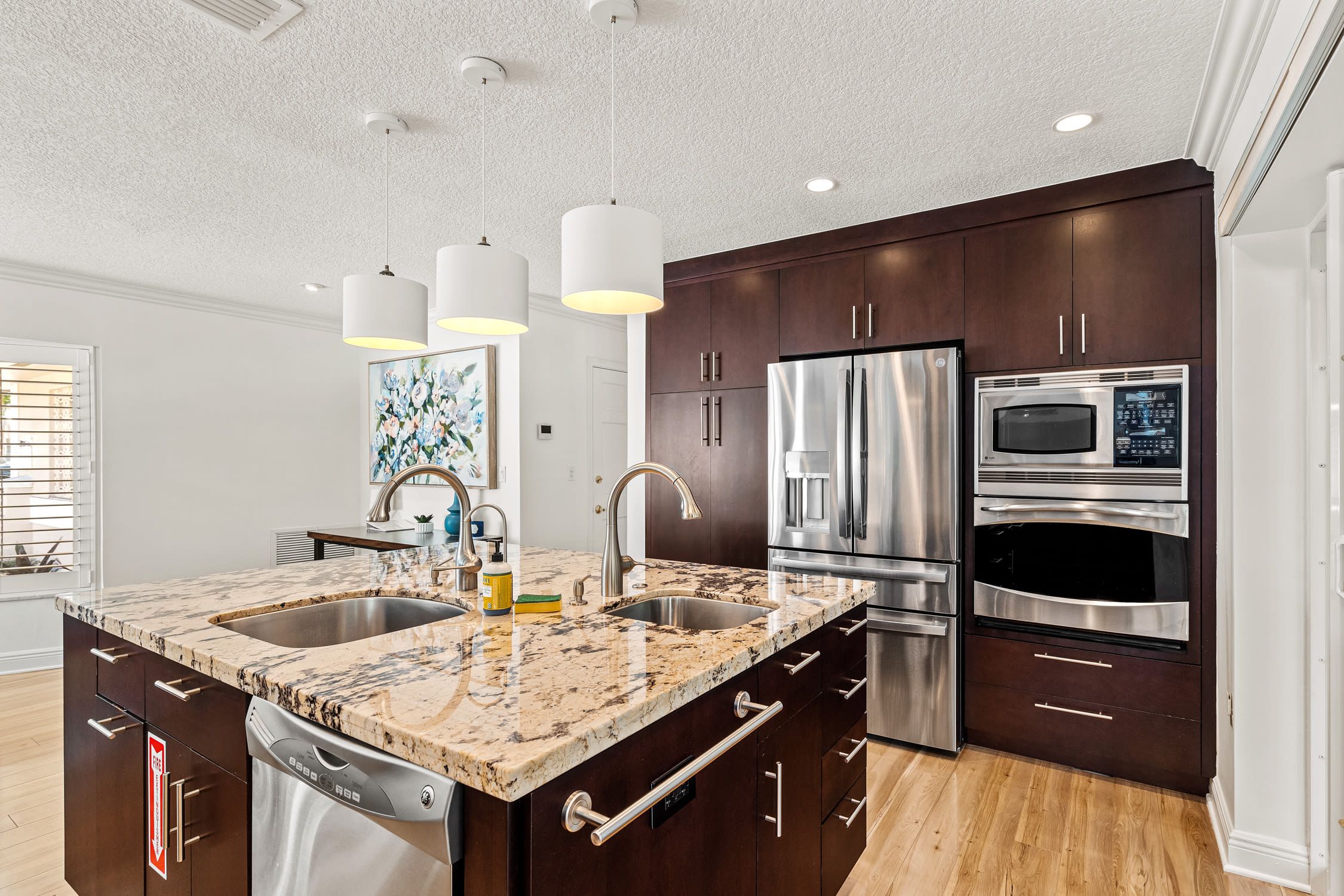 A modern kitchen with a double sink, stainless steel appliances, and dark wood cabinets.
