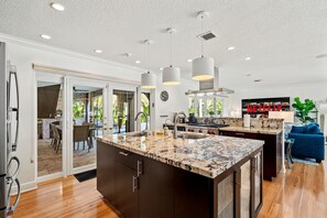 Een moderne keuken met een groot eiland, hanglampen en uitzicht op een terras.